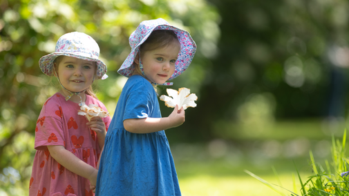 Two little twin in floral dresses hold a flower in the spring sunshine at Saltram